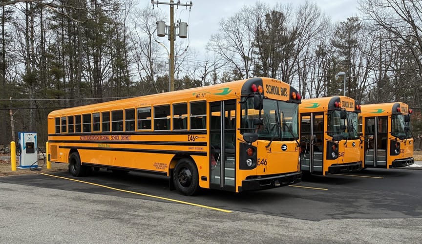 Three school buses parked in a lot and connected to a charger