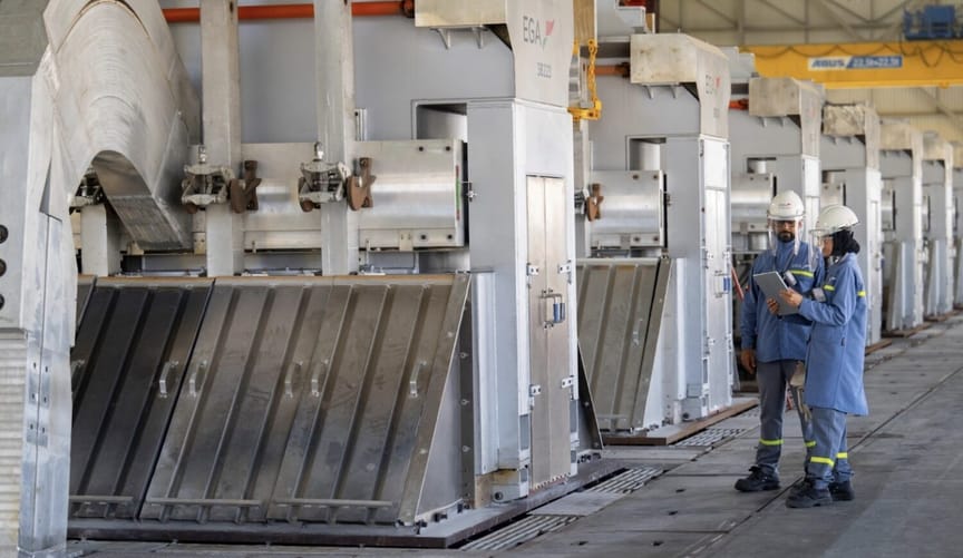Two people in blue work gear and white hard hats hold clipboards next to a row of industrial equipment labeled EGA