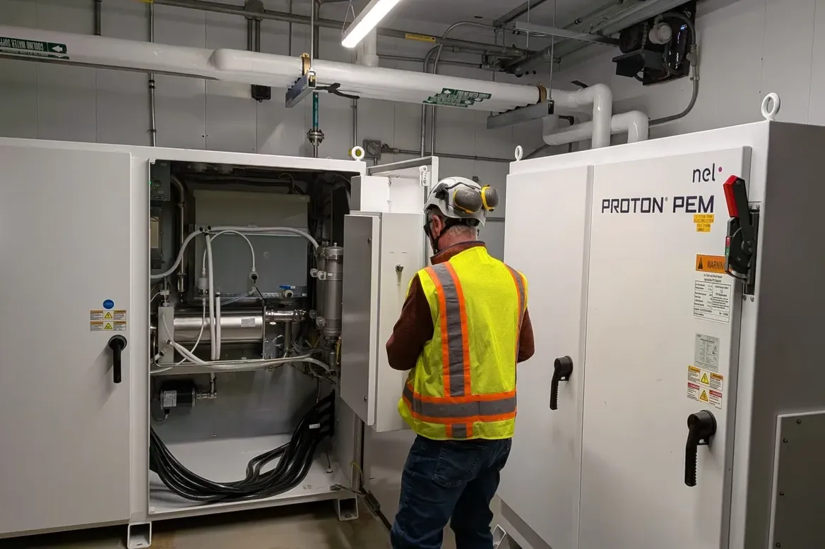 A safety-vested worker from the back in front of a open equipment door