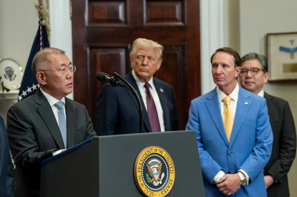 Man in suit at a podium with the presidential seal, along with three other men in suits