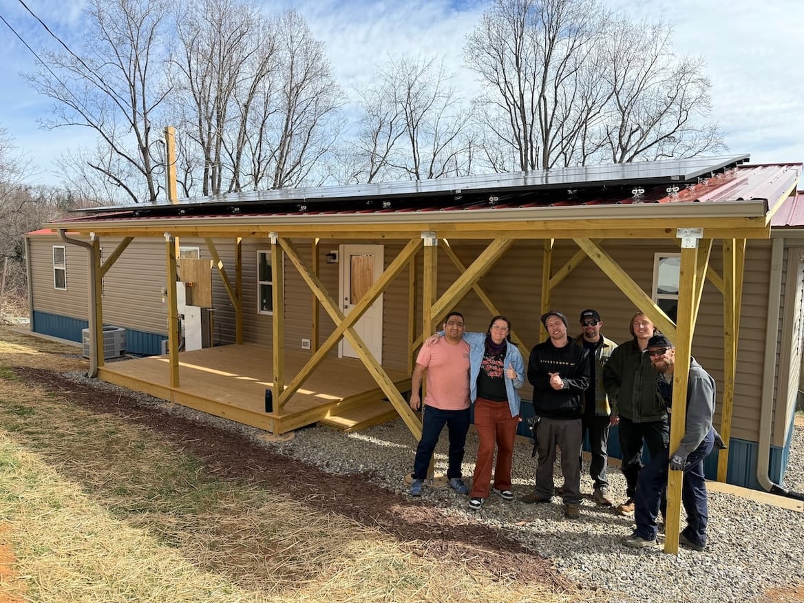 Six people standing in front of a manufactured home with a porch built to hold solar panels
