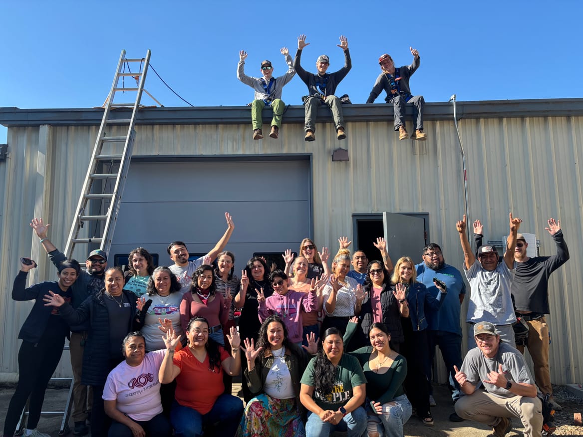 Group of people in front of a building and three on the roof, hands in air