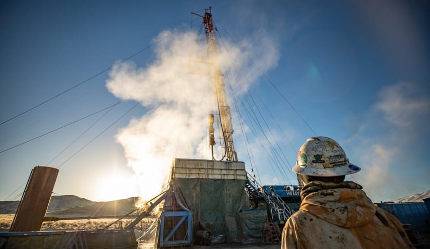 POV from behind a worker walking toward a geothermal equipment steaming under a blue sky