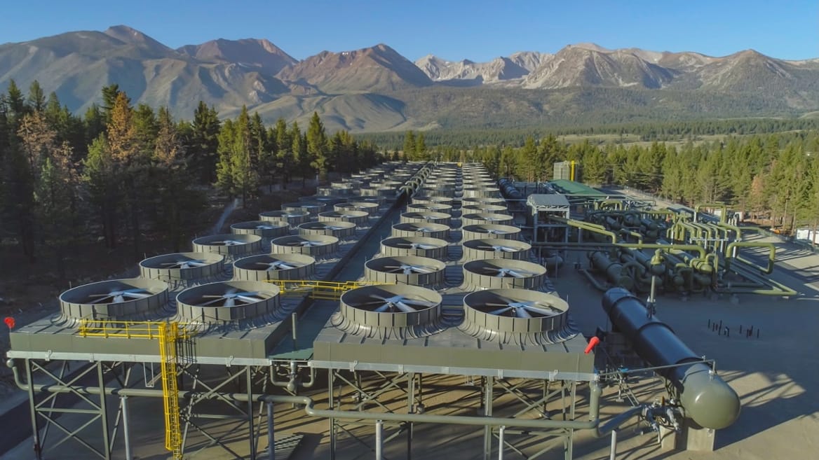 Overhead of geothermal plant surrounded by trees with mountains behind