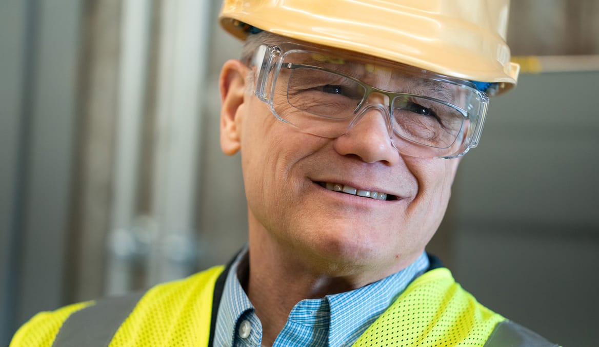 Man in safety hat and glasses with yellow safety vest and blue collared shirt