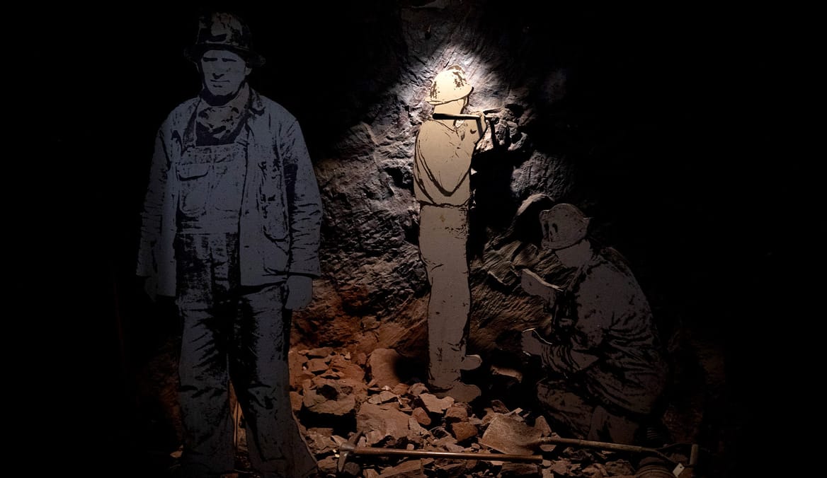 2D cutouts of miners standing by a rock wall