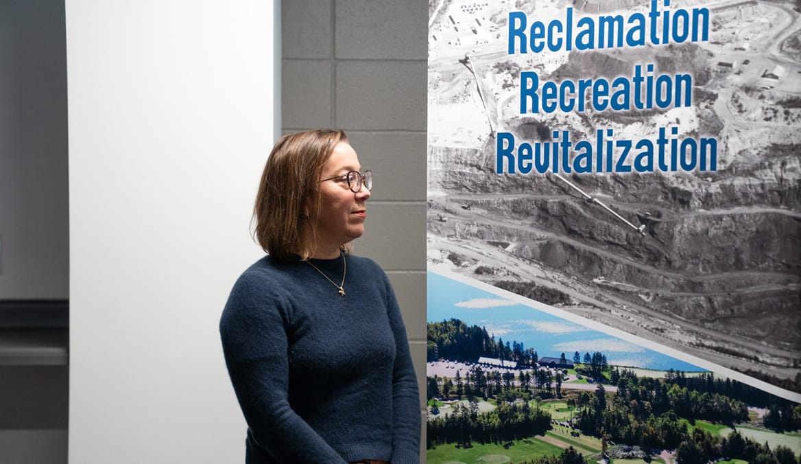 Woman in blue top standing by poster with "Reclamation, Recreation, Revitalization"