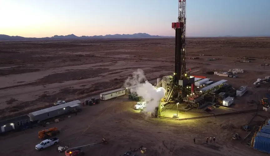 Geothermal well site at at dusk or sunrise, with a lights shining on worksite