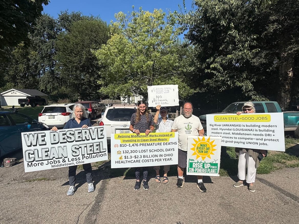 Five people holding signs asking for clean steel; cars and trees behind them