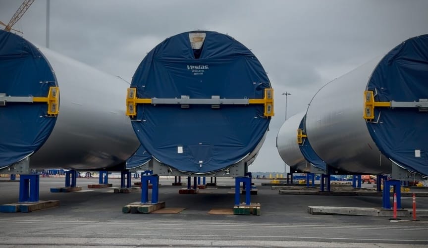 White wind turbine parts on a concrete lot; blue material covering the end