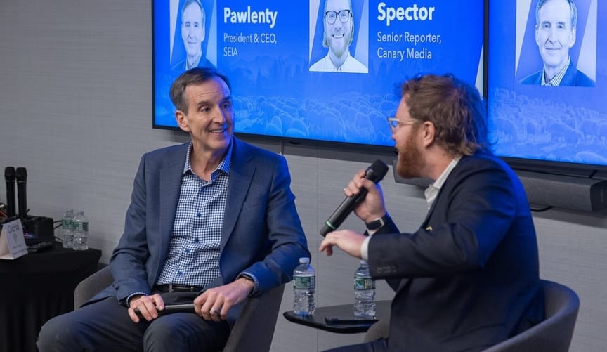 Two men sit in chairs, both in suits, one on the right holding microphone; background has names and images: Pawlenty, Spector