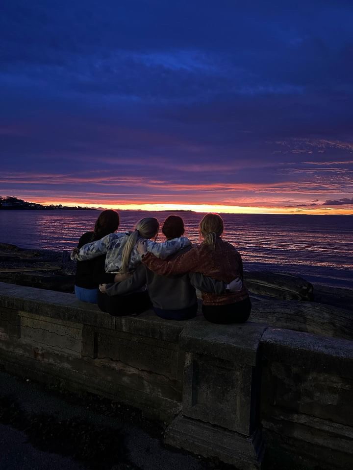 Group of friends sitting on rocks watching the sunset over the water