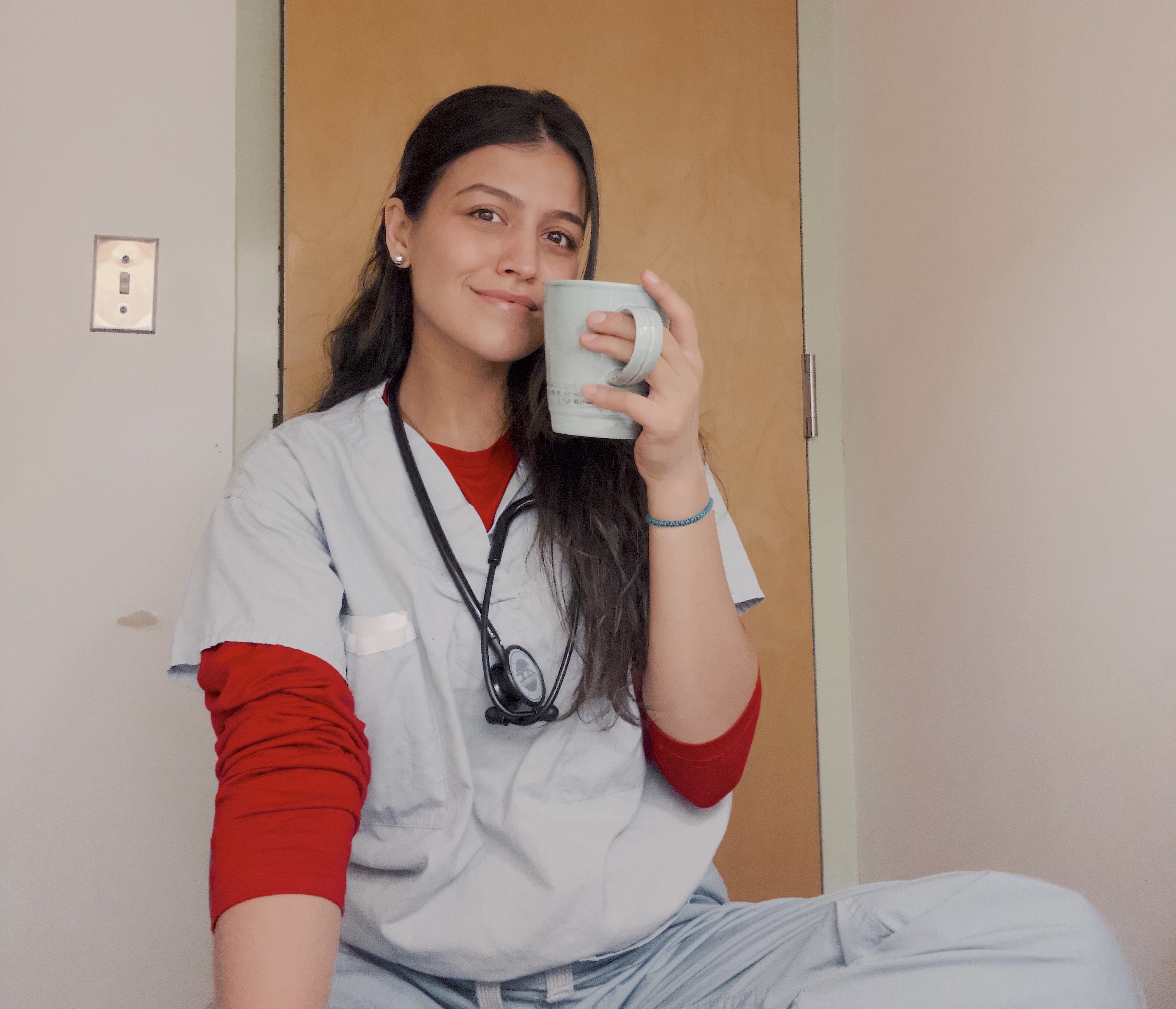 Nurse in scrubs smiling and holding a coffee mug