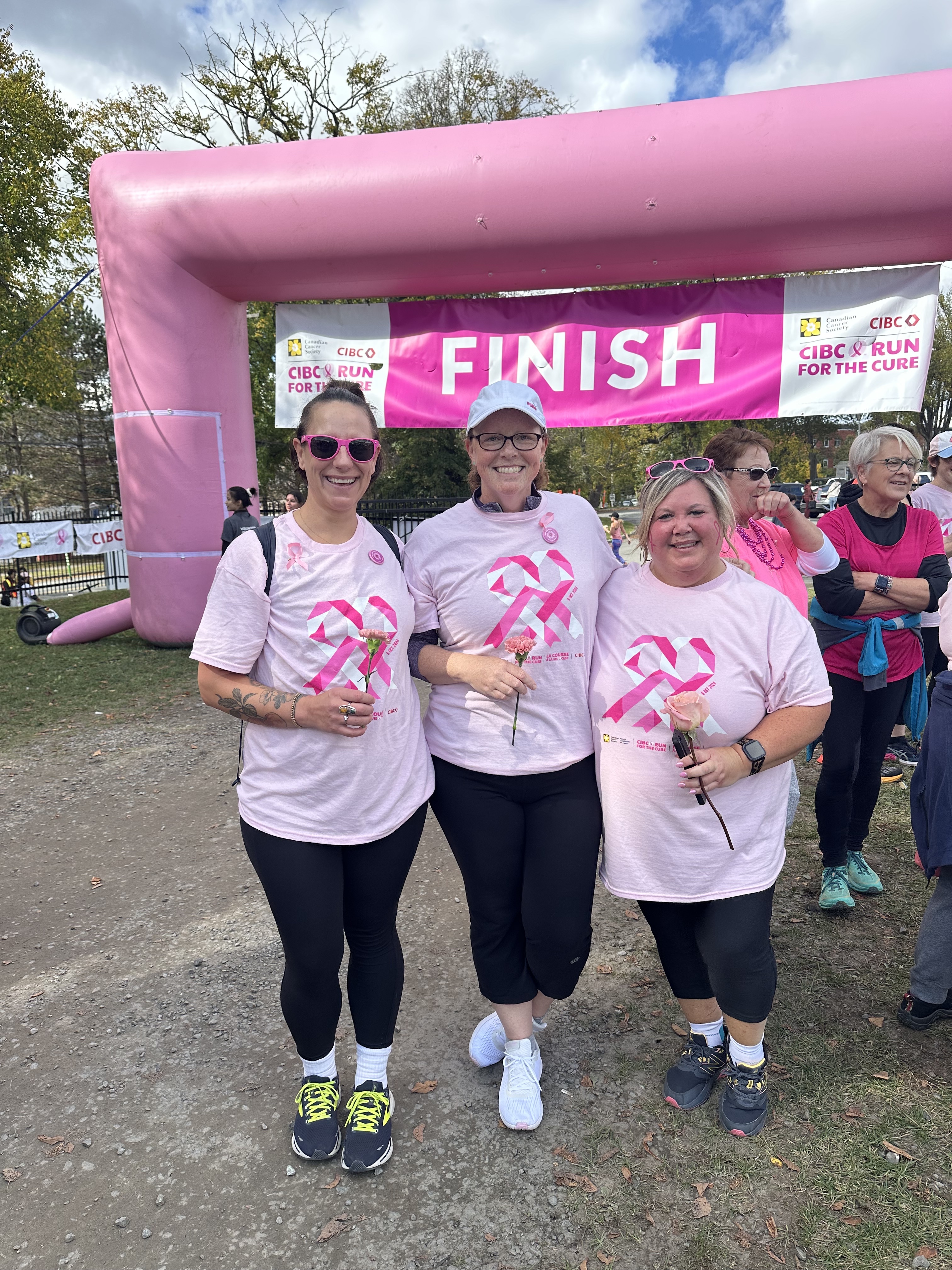 Three women in pink t-shirts celebrating in front of a pink inflatable finish-line arch at a charity run