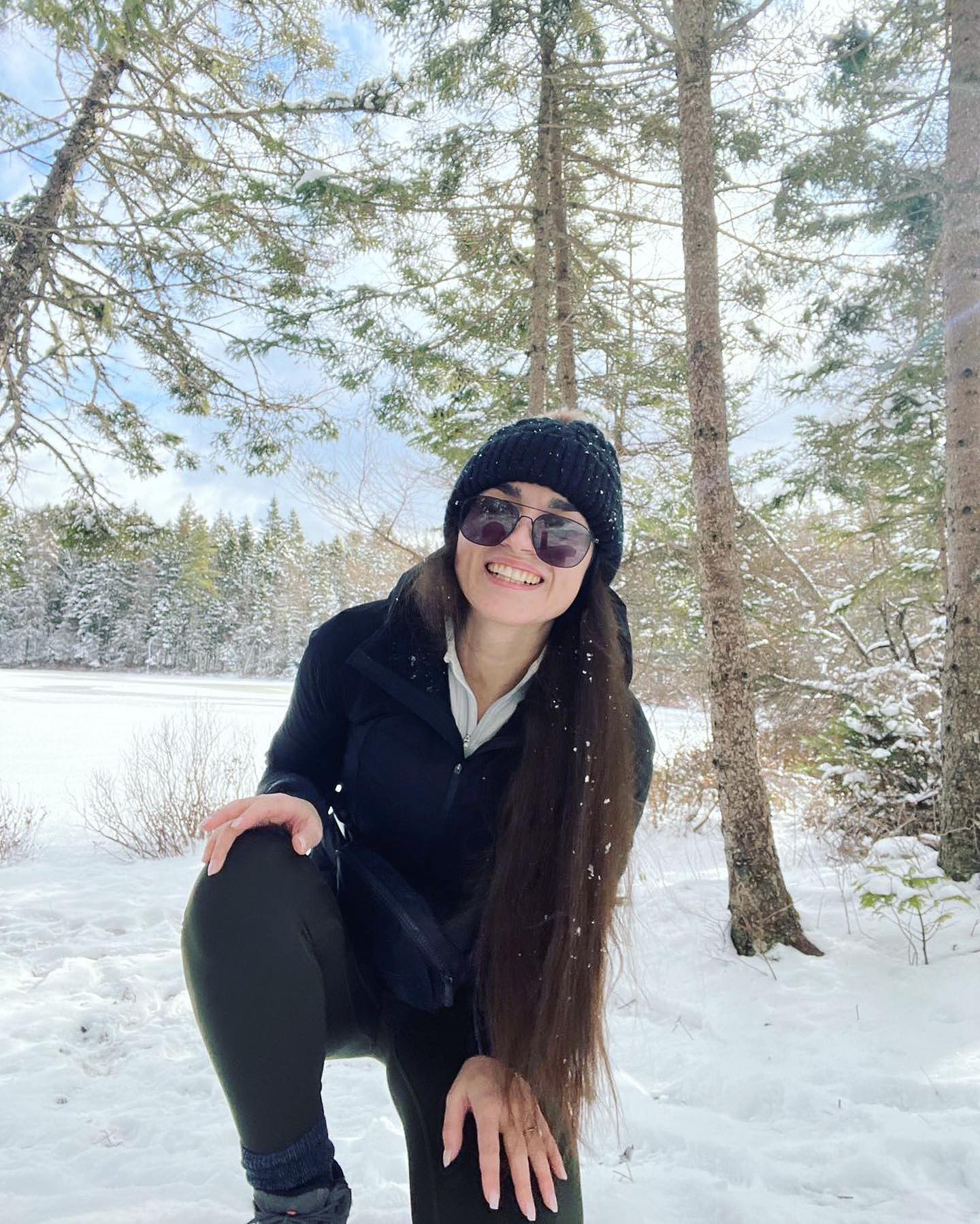 Smiling woman in a winter jacket and toque crouching in a snowy forest