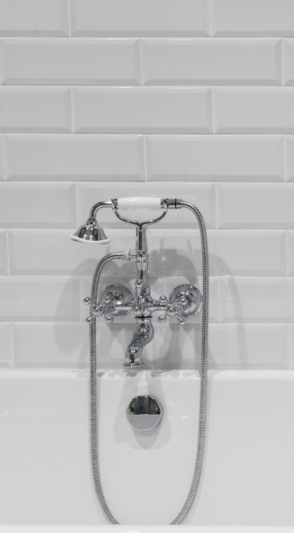 A vintage-style chrome bathtub faucet and handheld shower head mounted against a white subway tile wall.