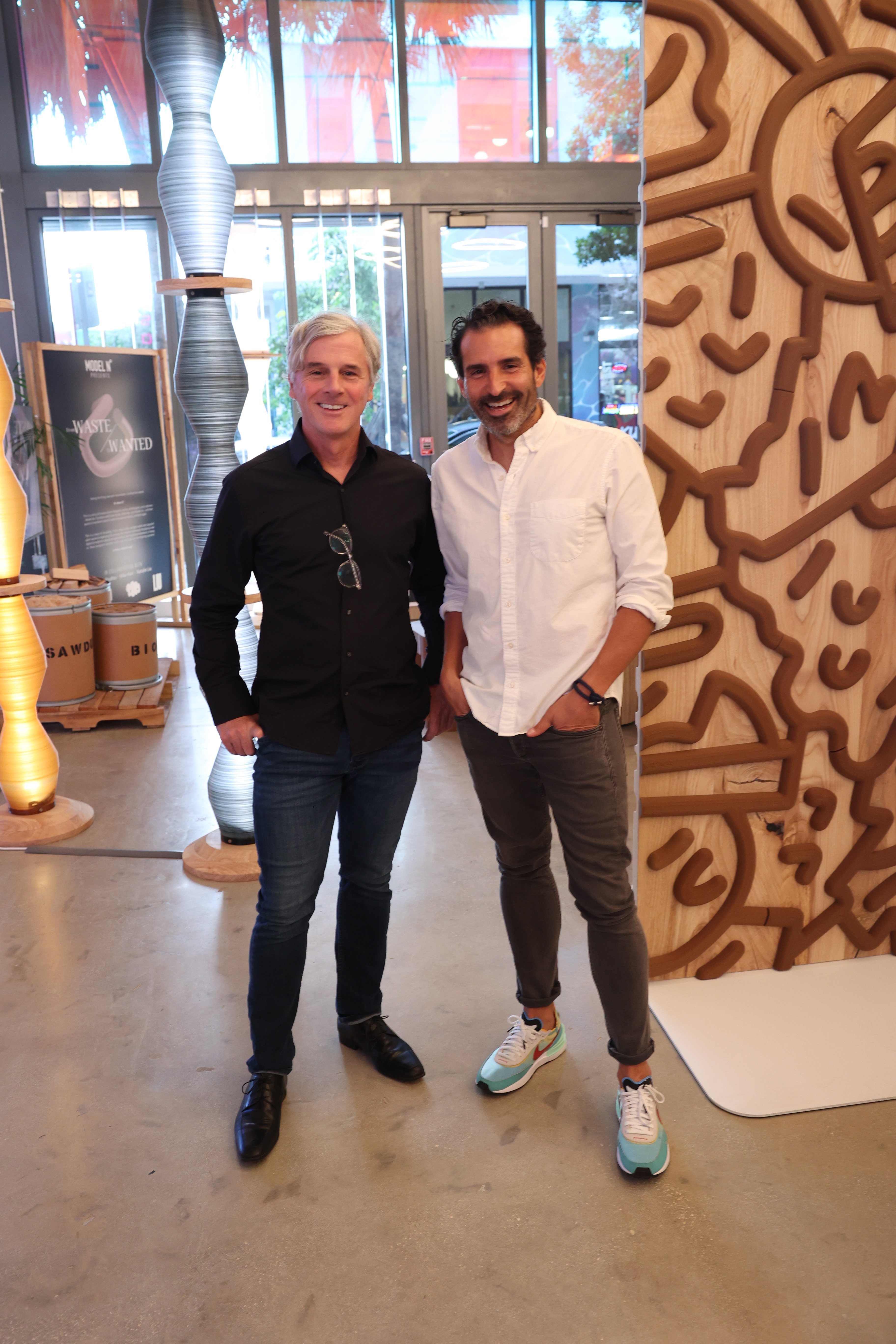 A picture of two men in a bright lit room with artistic creations surrounding them