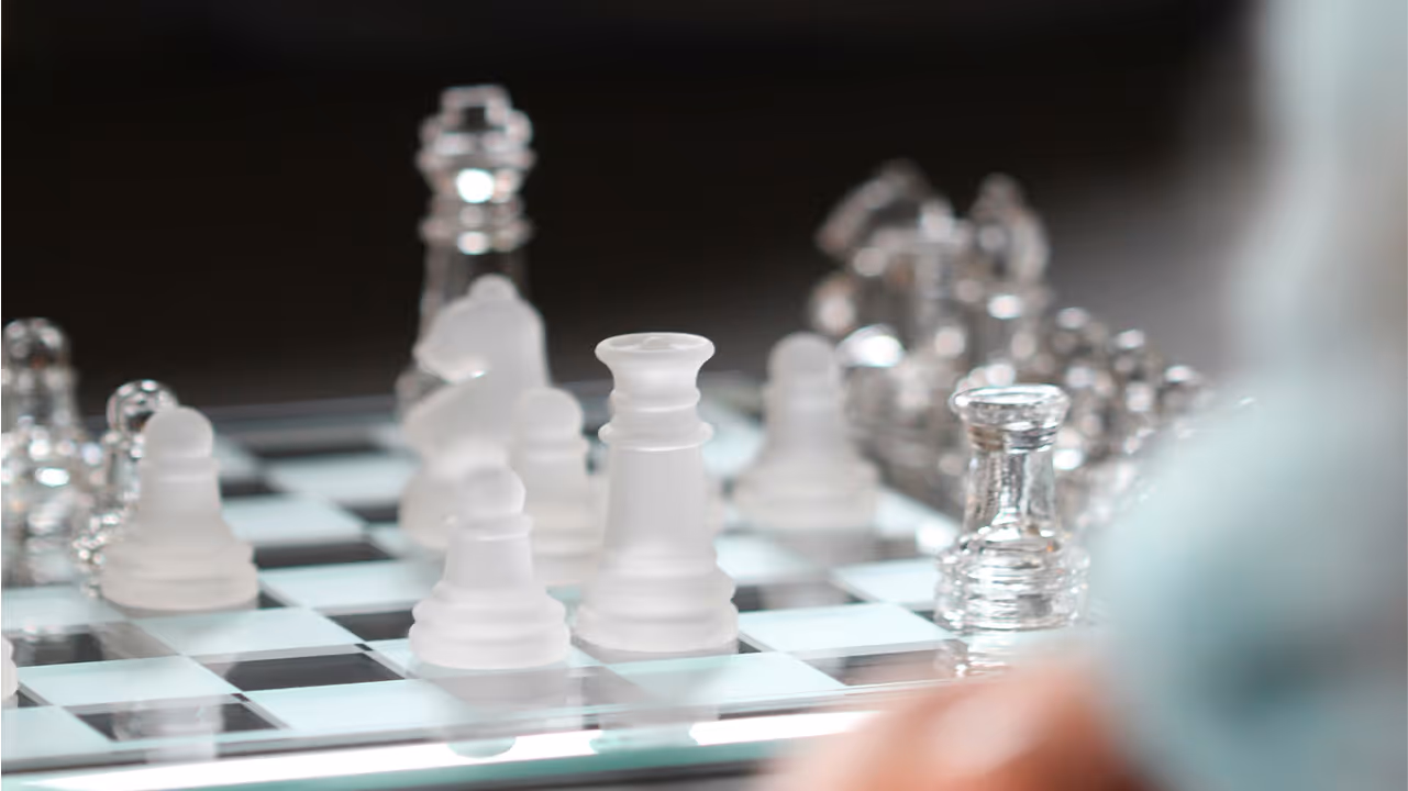 A hand is touching a glass chess board with pieces.