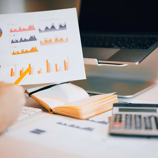 A person is holding a book with graphs and a calculator on a desk.