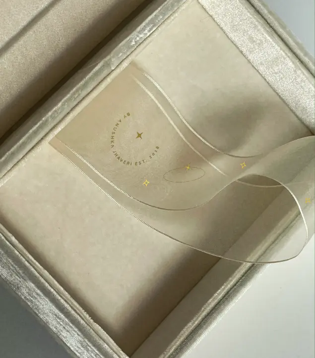 This image captures a Golden Gazelle jewellery box, designed in soft champagne velvet with an elegant translucent ribbon featuring the brand’s insignia and delicate gold accents. The refined detailing and gentle textures embody Golden Gazelle’s design ethos—quiet luxury, authenticity, and emotional connection. The subtle shimmer of the materials and minimal aesthetic evoke a sense of ceremony and care, reflecting the brand’s commitment to crafting jewellery that feels personal, meaningful, and timeless.
