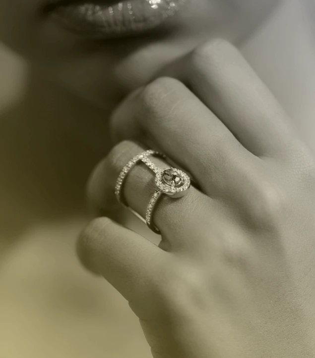 This close-up captures the elegance of a handcrafted diamond ring from Golden Gazelle, highlighting its double-band design adorned with pavé-set diamonds and a central halo setting. The soft, sepia-toned lighting enhances the ring’s intricate detailing, reflecting timeless luxury and fine craftsmanship. The composition evokes intimacy and sophistication, staying true to Golden Gazelle’s philosophy of creating jewellery that embodies authenticity, emotion, and understated opulence.
