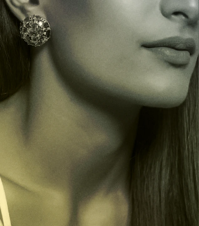 This close-up photograph highlights an elegant woman wearing statement earrings. The image focuses on the jawline, neck, and lower half of the face, showcasing the intricate detailing of the circular earring with embedded stones. The lighting is warm with a greenish-gold tone that adds a sophisticated, timeless aesthetic. The composition draws attention to texture, contrast, and minimalism, making it ideal for use in luxury fashion, jewellery, or editorial branding contexts.
