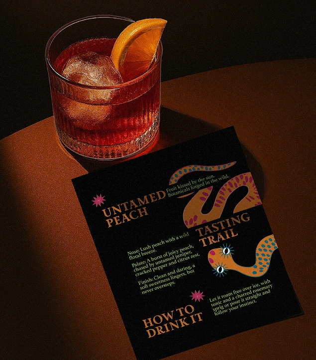 Beverage branding and promotional design for Untamed Gin by Dot and Grid – moody tabletop shot with an amber cocktail and tasting card for the ‘Untamed Peach’ variant. Features colourful snake illustration, elegant typography, and luxury alcohol packaging storytelling.