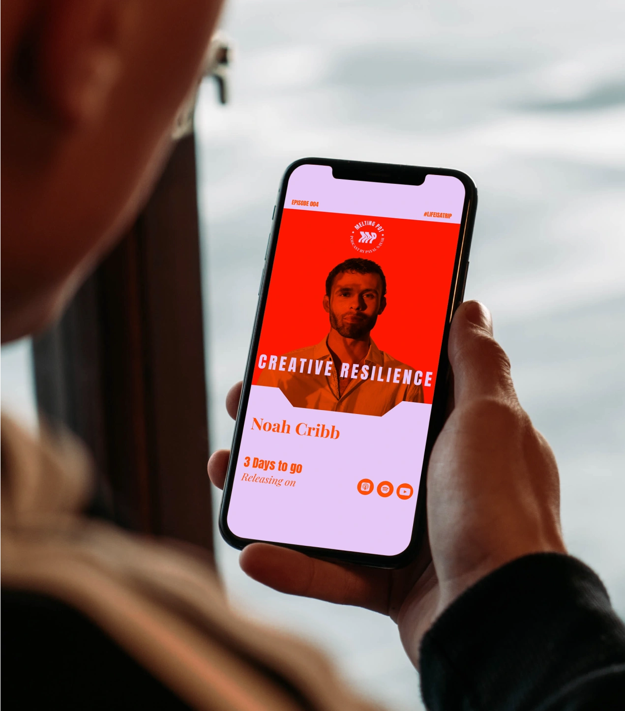 A listener viewing the Melting Pot Podcast episode “Creative Resilience” featuring Noah Cribb on a smartphone screen. The vibrant red and lilac interface design conveys the podcast’s bold visual identity and focus on stories of creativity, perseverance, and cultural impact in a digital-first listening experience