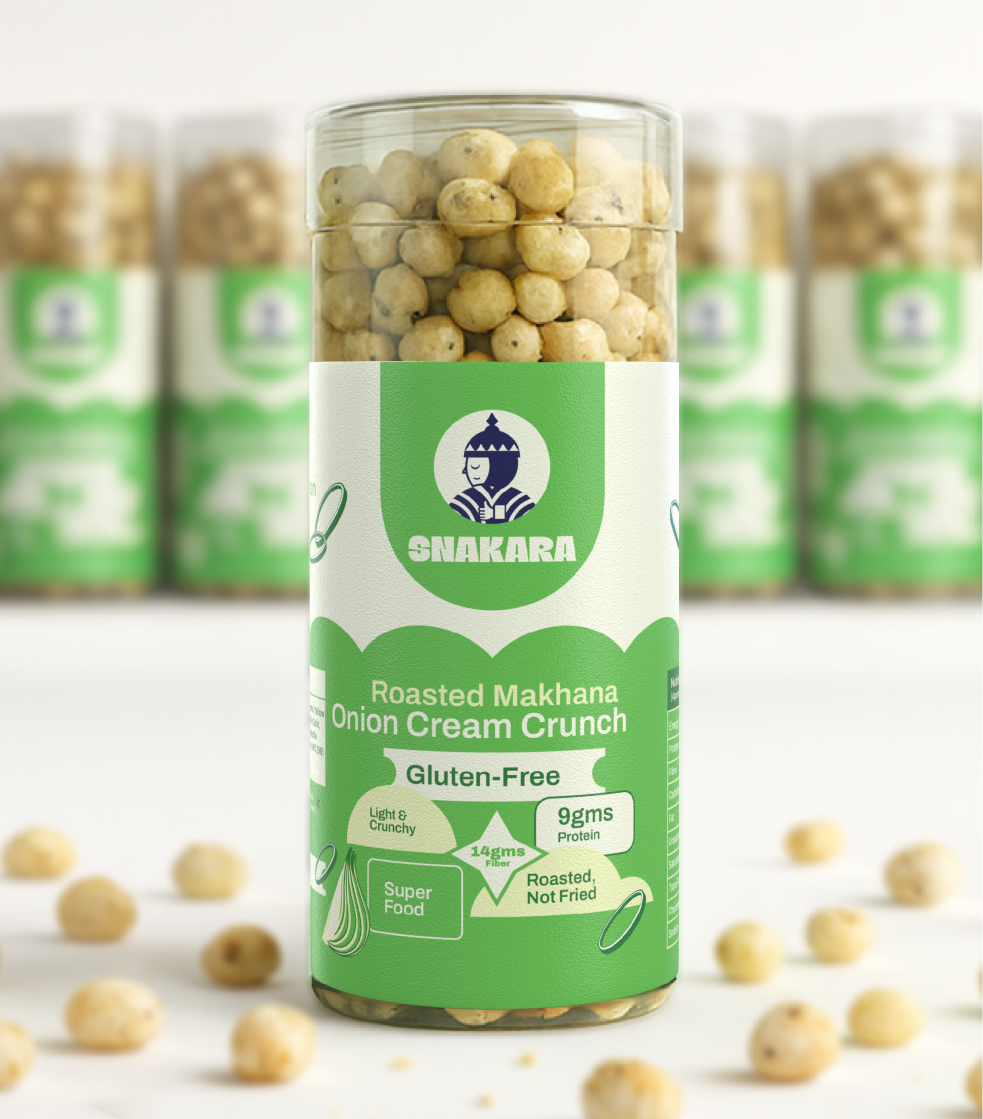 This image highlights **Snakara’s Roasted Makhana – Onion Cream Crunch** in its signature cylindrical jar. The packaging design balances health cues with modern aesthetics, using a fresh green and cream palette that communicates lightness and flavor. The front label features Snakara’s Samurai emblem — a symbol of discipline and mindful eating — along with clear nutritional highlights: *Gluten-Free, 9g Protein, 14g Fiber, Roasted Not Fried, Superfood.*

The matte texture, rounded typography, and minimal graphics give the pack a clean, premium look while staying approachable. Surrounded by scattered makhanas, the composition reinforces the brand’s promise of *healthy snacking made joyful*, designed for those who crave flavor without compromise.
