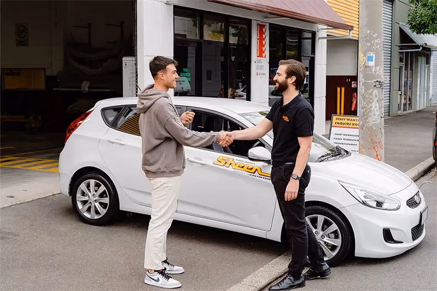 Sheen worker and customer shaking hands, customer is getting a temporary Sheen vehicle. 