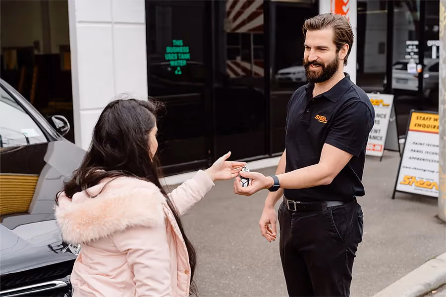 Woman in pink coat handing over keys to male Sheen worker.
