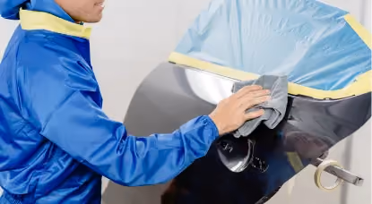 Technician preparing and polishing car panel during vehicle refinishing process.