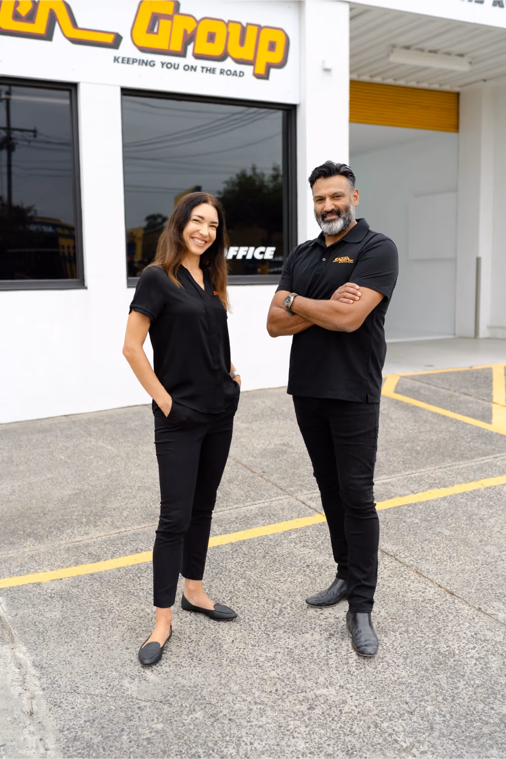 Two Sheen Group staff members standing outside a service centre, smiling confidently in black uniforms.