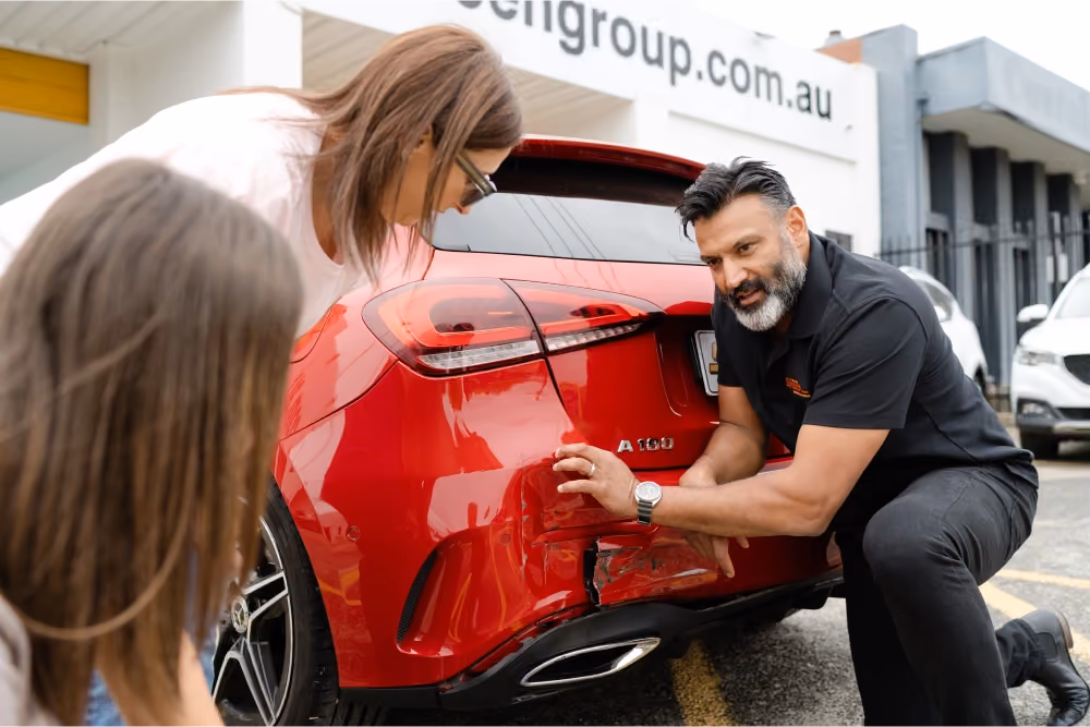 Sheen Group staff member showing rear-end damage on a red car to two customers outside the service centre.
