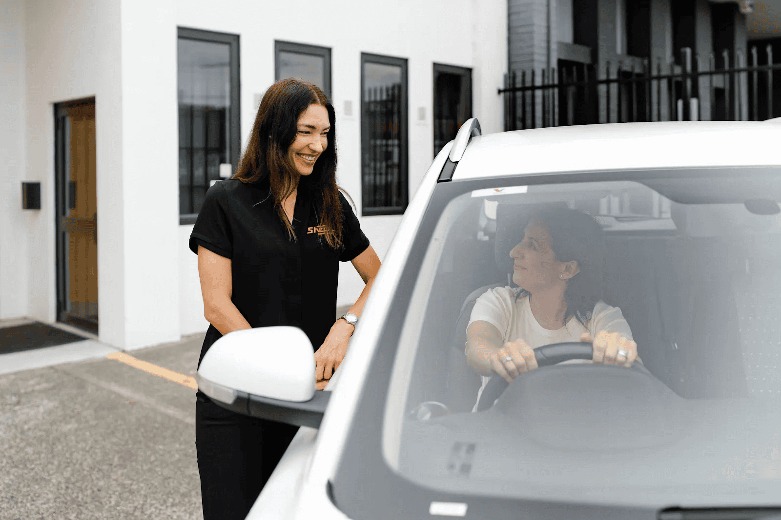 Sheen staff member smiling and speaking with a woman sitting in the driver’s seat of a white SUV outside a repair centre.