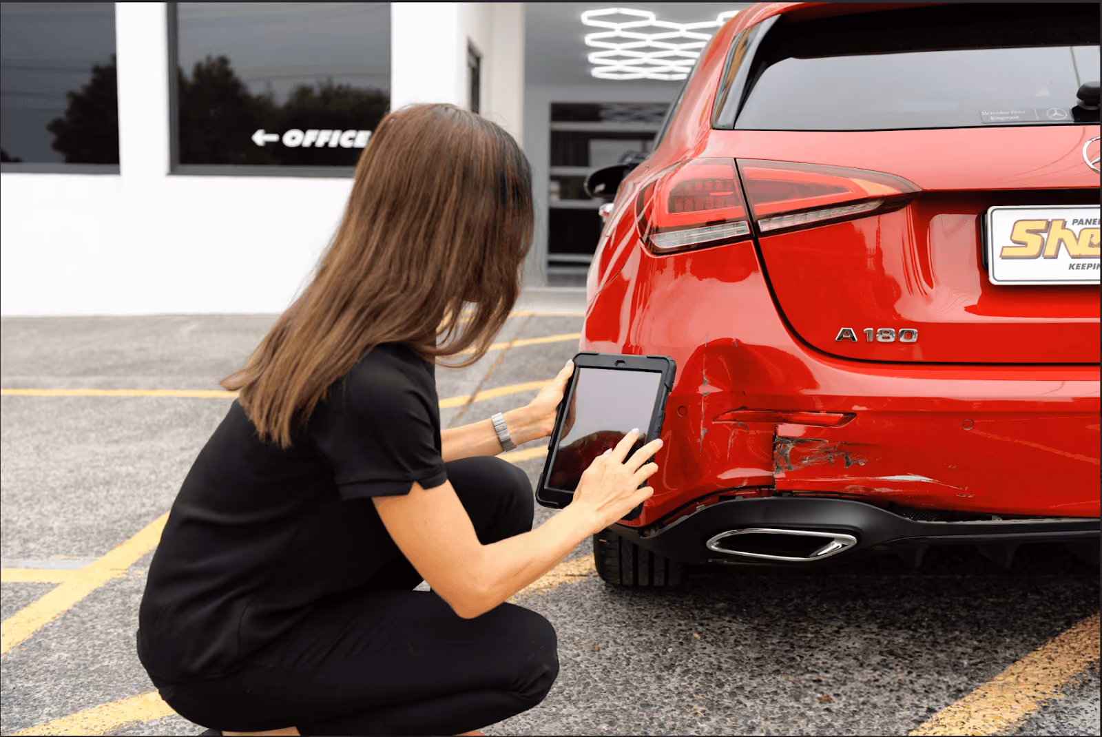 Sheen Panel Service technician inspecting bumper damage on a red car.