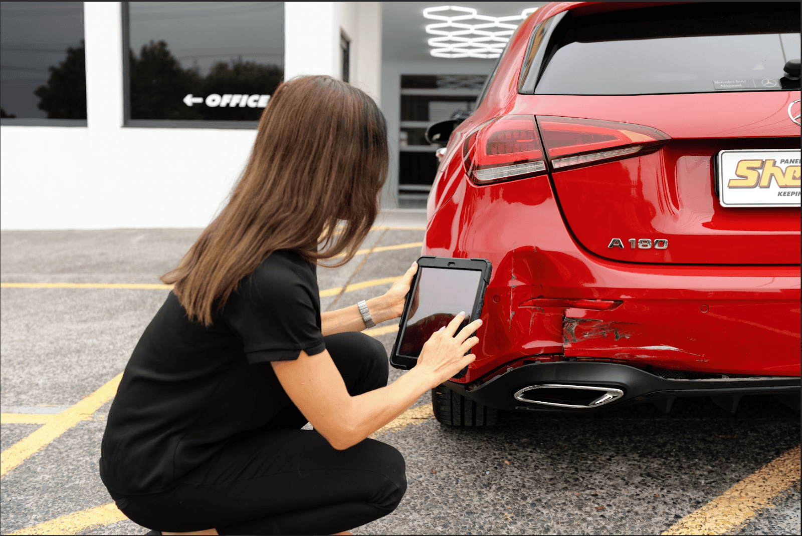 Sheen Panel Service technician inspecting bumper damage on a red car.