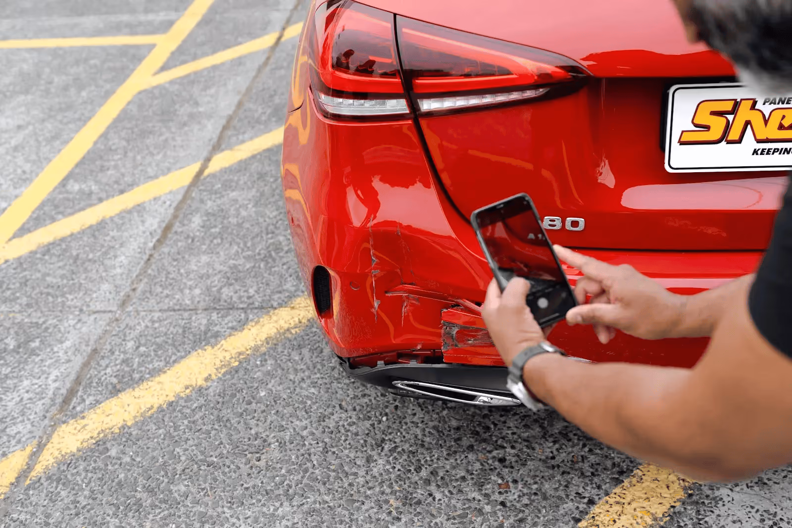 Person taking a photo of rear-end damage on a red car to document the accident for an insurance claim.