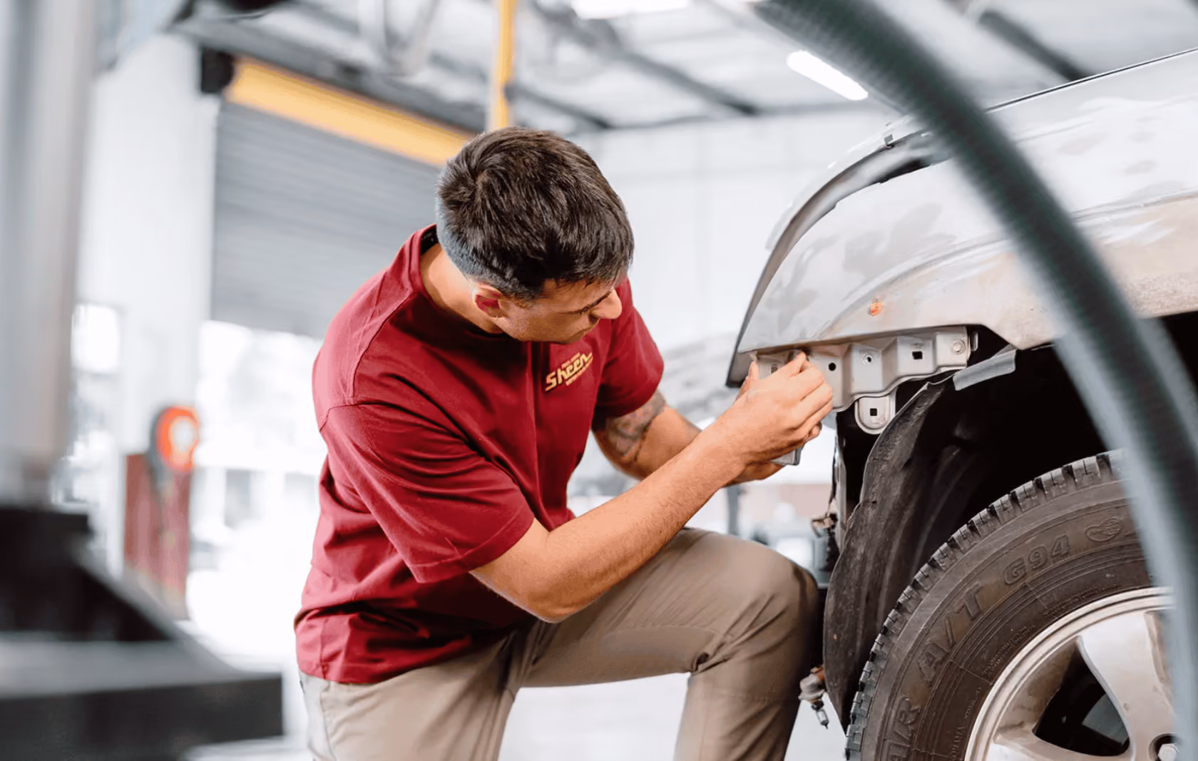 Sheen technician inspecting and repairing the front wheel arch panel of a car inside a smash repair workshop