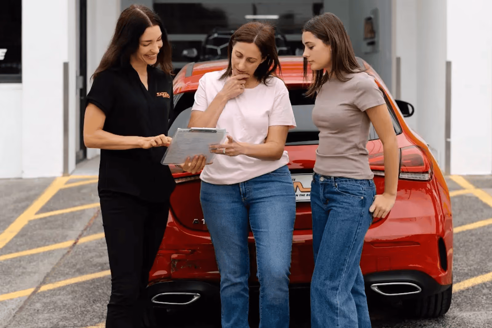 Sheen team member assisting two women with insurance paperwork near a red car after an accident.