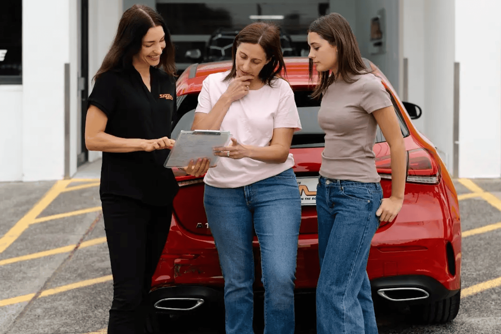Sheen team member assisting two women with insurance paperwork near a red car after an accident.