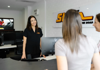 Sheen panel beating staff member welcoming customers at the reception desk, providing advice on smash repairs and questions to ask your panel beater.
