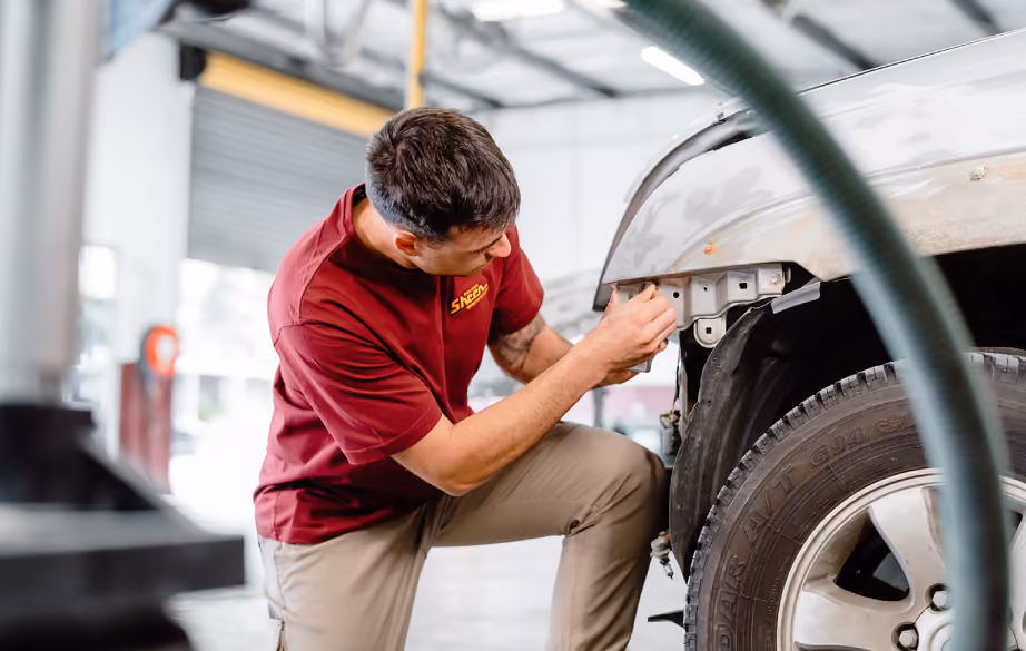 An auto repair technician examining and aligning a damaged car panel inside a workshop.