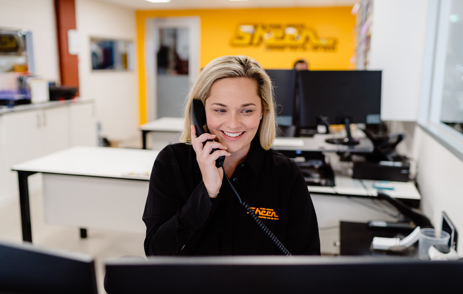 A friendly Sheen Group receptionist speaking with a customer over the phone, assisting with a car accident claim process at the front desk.