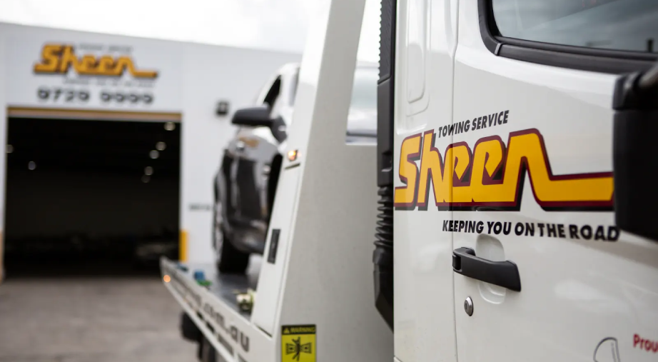 Sheen tow truck carrying a vehicle outside the Sheen workshop, ready for towing service.