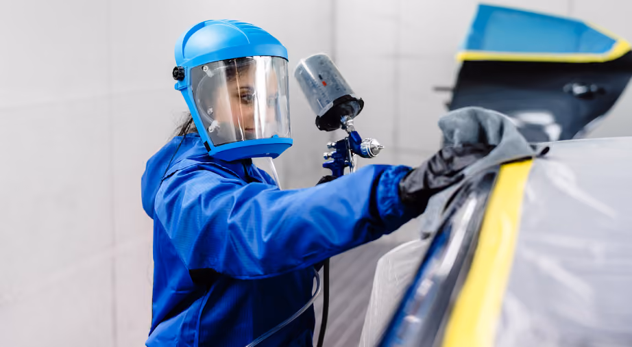 Panel beater spray painting car panel in controlled workshop environment.