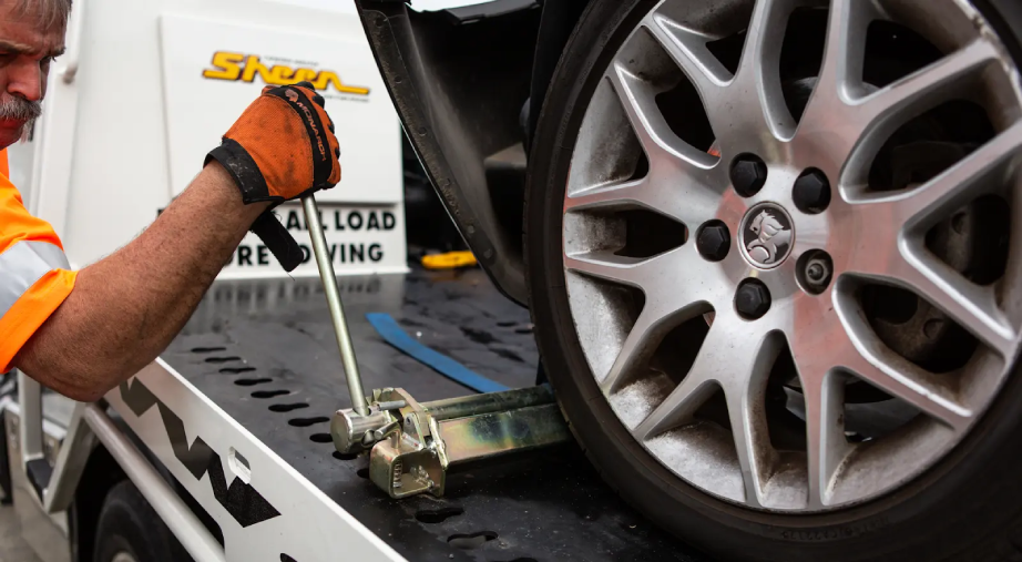 Technician securing vehicle wheel on Sheen tow truck tray.