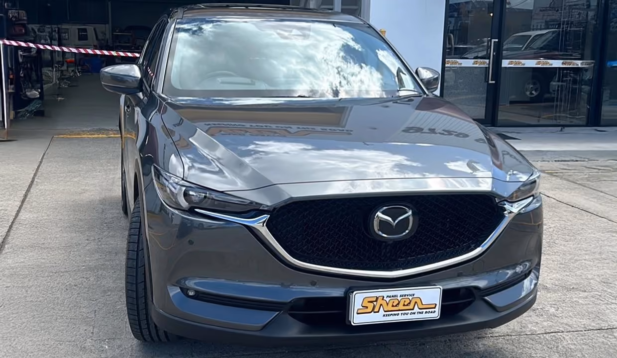 Front view of a grey Mazda CX-5 after repair, with a clean, aligned bumper and grille, restored to like-new condition outside a workshop.
