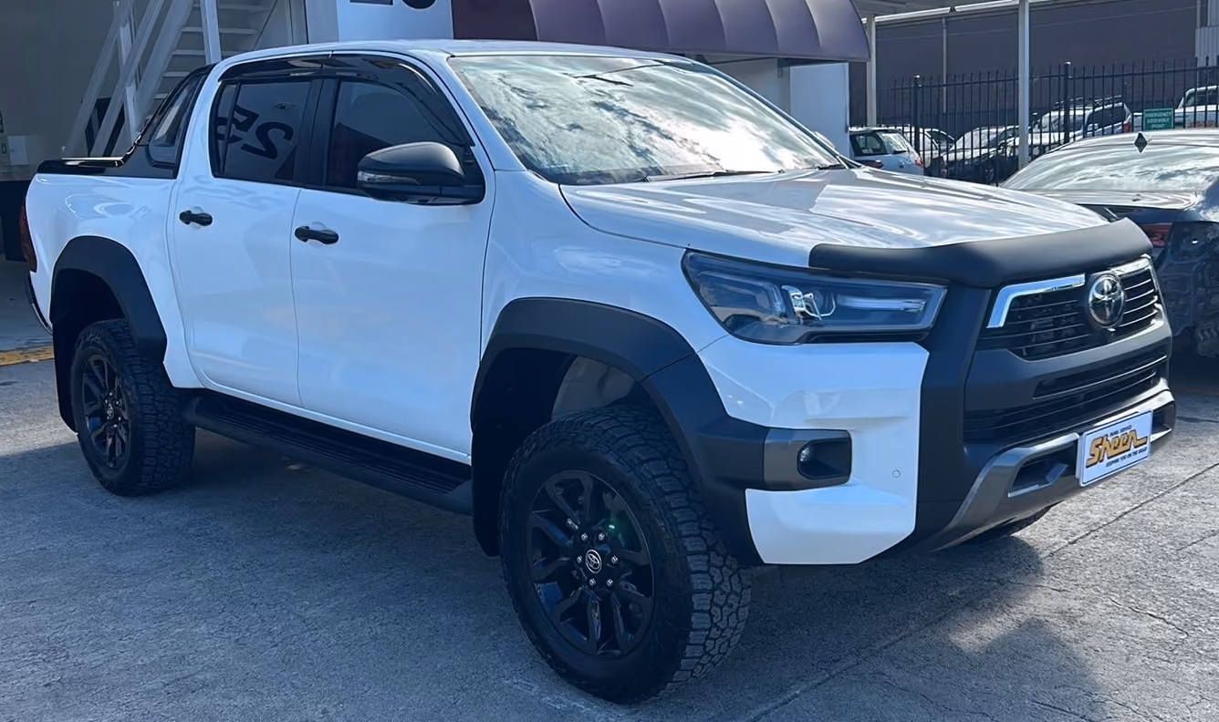 Front-side view of a white Toyota Hilux after repair, with smooth, restored panels and no visible damage, parked outside a workshop.