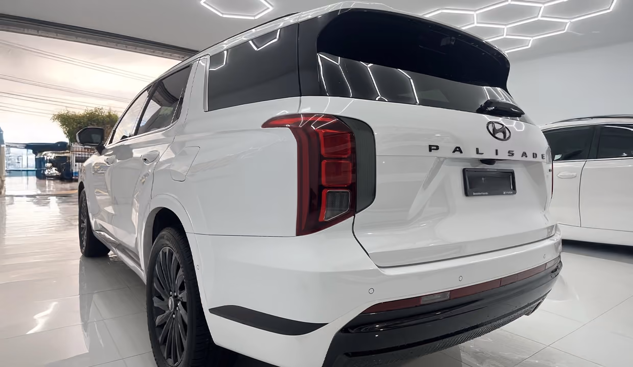Rear-side view of a white Hyundai Palisade after repair, with the left rear panel fully restored, smooth bodywork, and no visible damage inside a workshop.